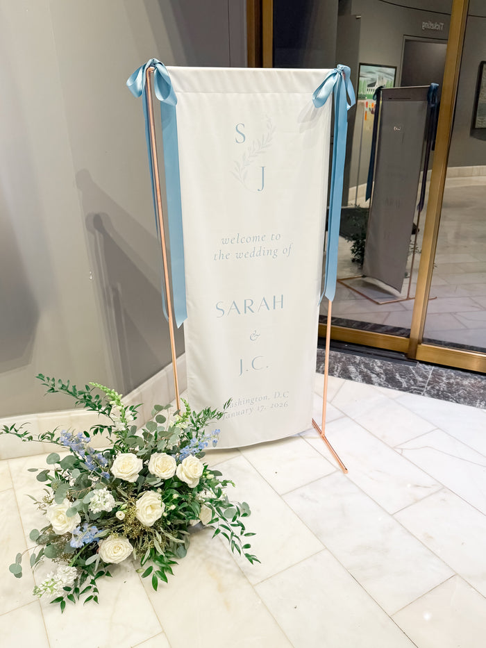 Floral arrangement in front of a decorative banner with text on a marble floor.